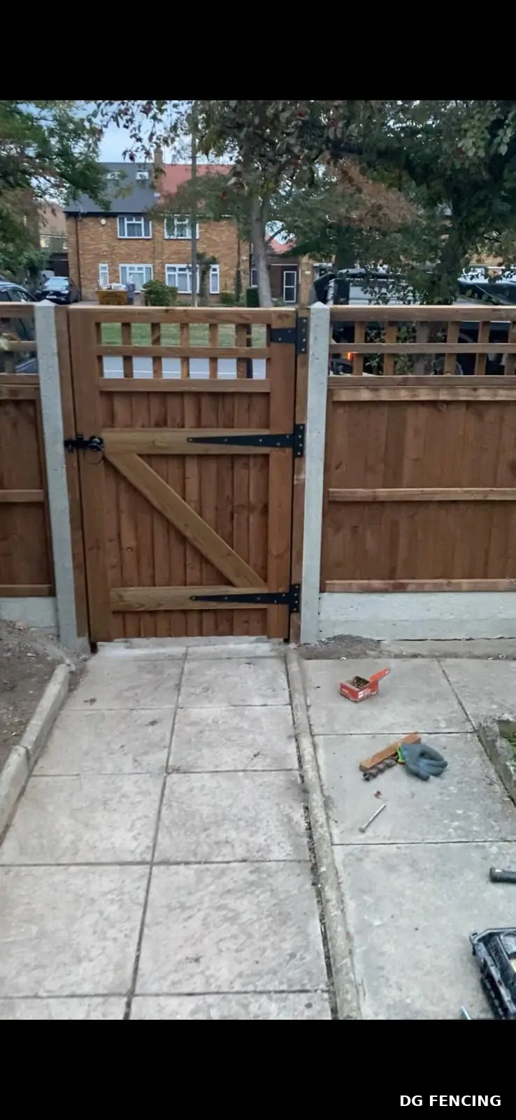 Timber garden gate with black hinges set between concrete posts and closeboard fencing